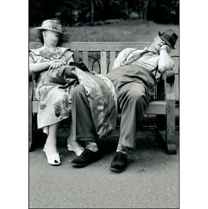 Front of card that shows a couple dressed in evening clothes, asleep on a bench. 