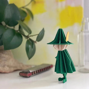 Snufkin is pictured standing next to a full-size harmonica amongst a plant. 